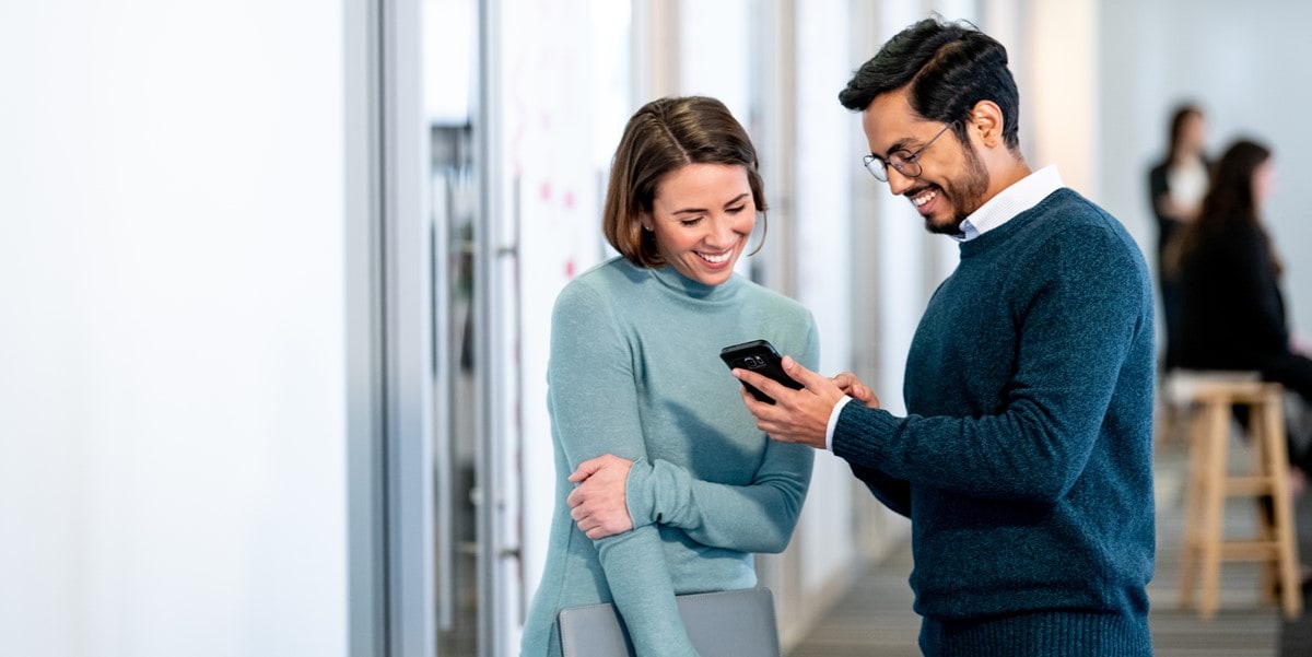 man showing cell phone to woman in office