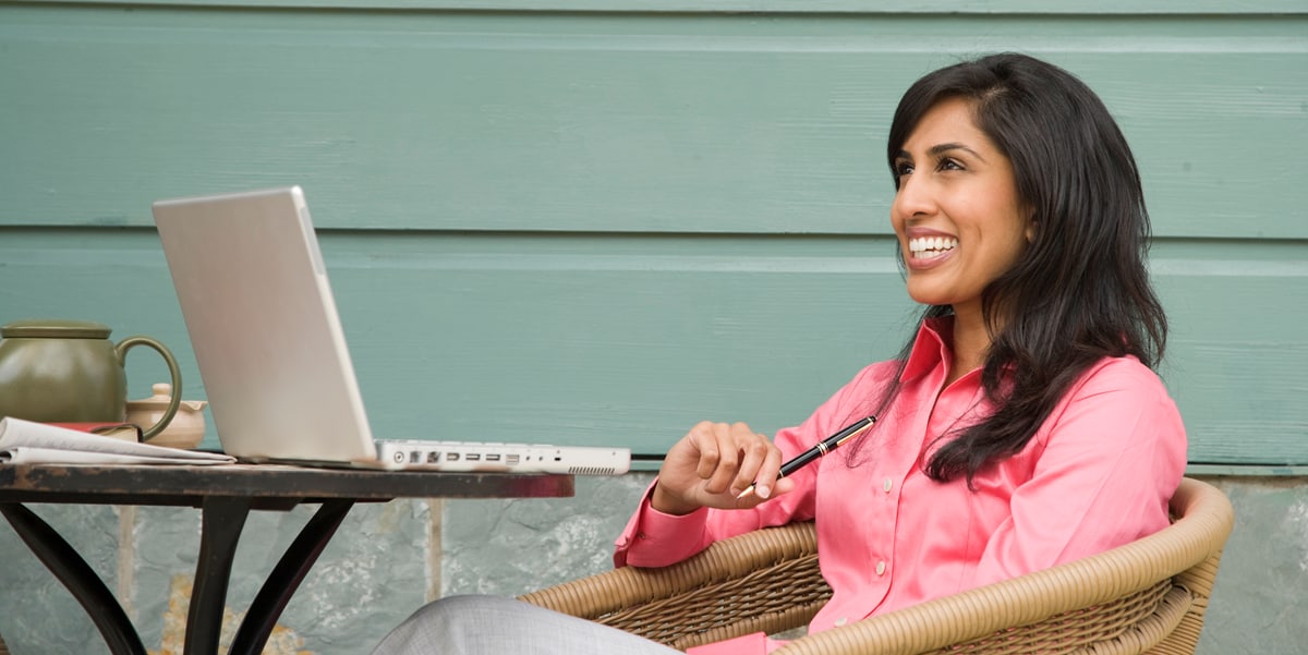 woman sitting at t able with a laptop, pen in hand