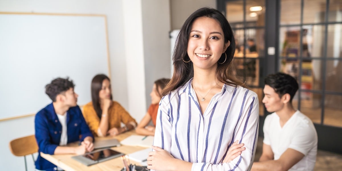 professional woman smiling, in the office, colleagues seated at table behind her