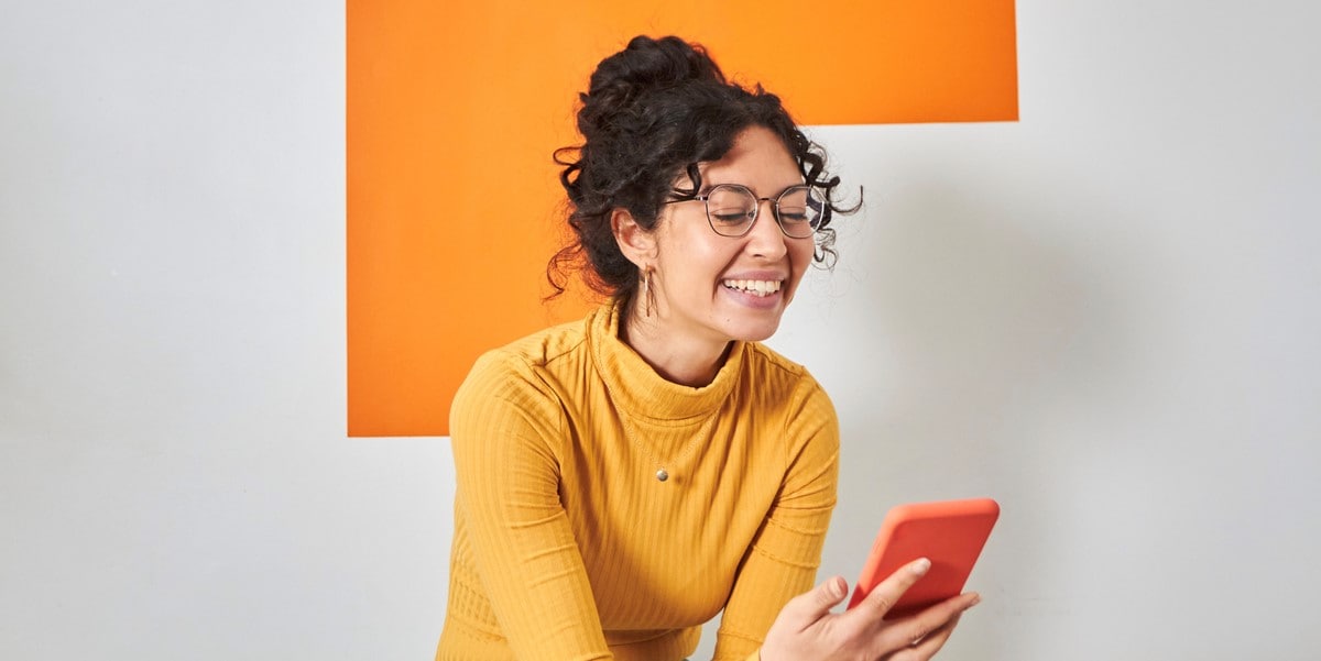 woman in orange top, looking down at cell phone