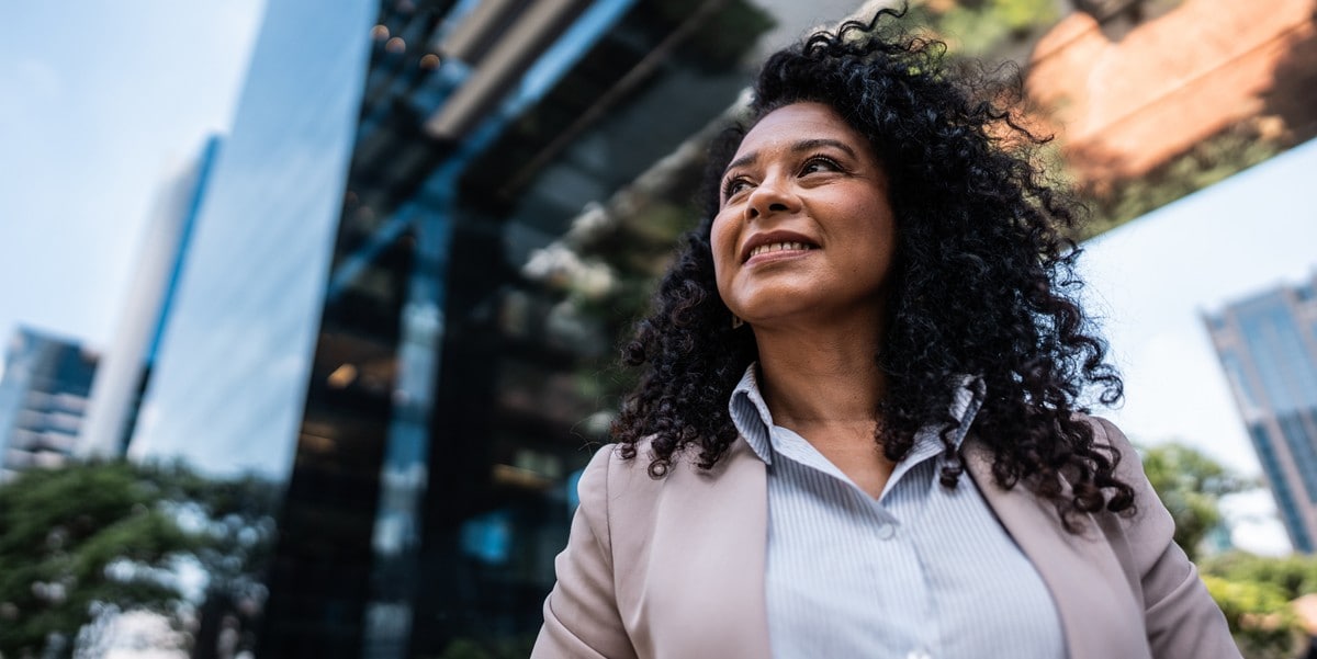 professional woman in a pink blazer smiling standing outside of an office building